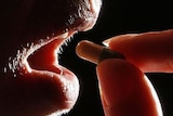 A person holds a pill up to their mouth.
