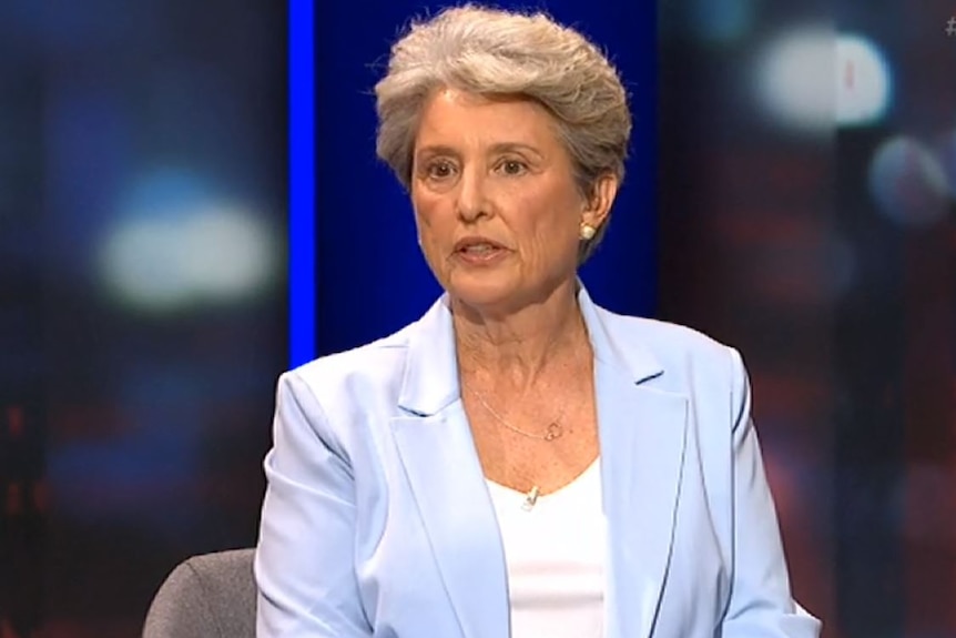 Kim Hoggard appears on Q+A wearing a light blue suit jacket, she has short grey hair.