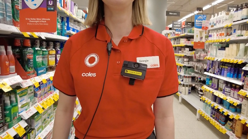 A close up of the torso of a Coles worker in a branded polo shirt, working in a store and wearing a body camera.