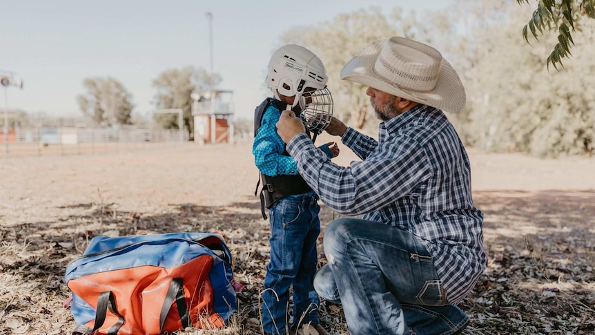 Older man helping young rider do up helmet.