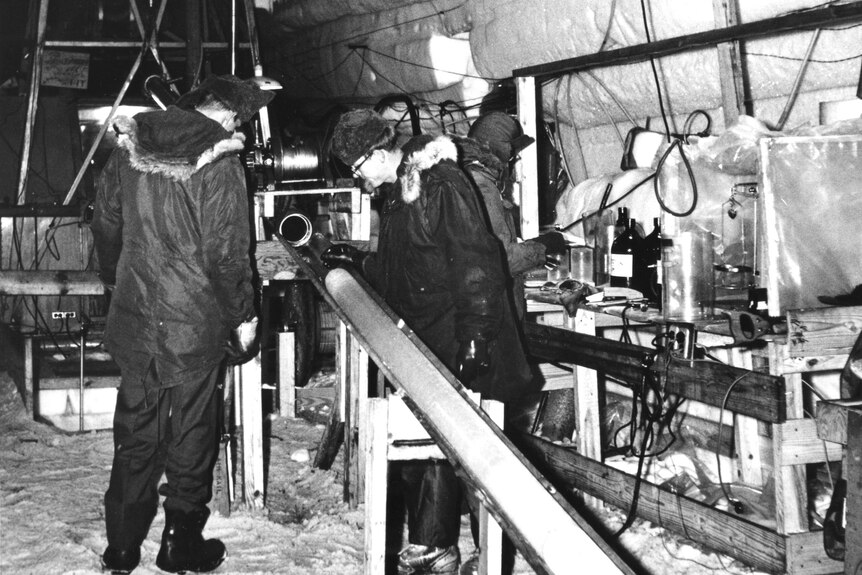 A black and white photo of researchers inspecting an ice core.