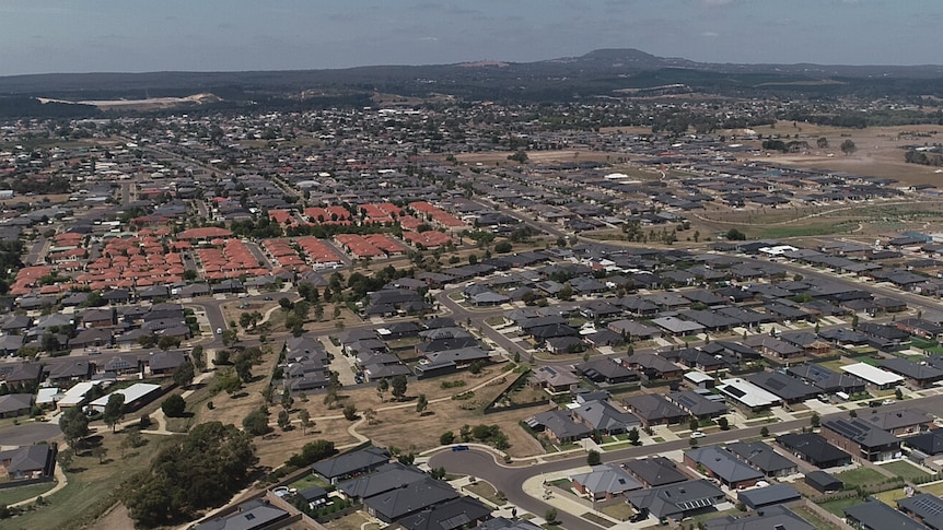 An aerial shot of a sprawling Australian suburb, most roofs are dark with a small patch of homes with red roofs.