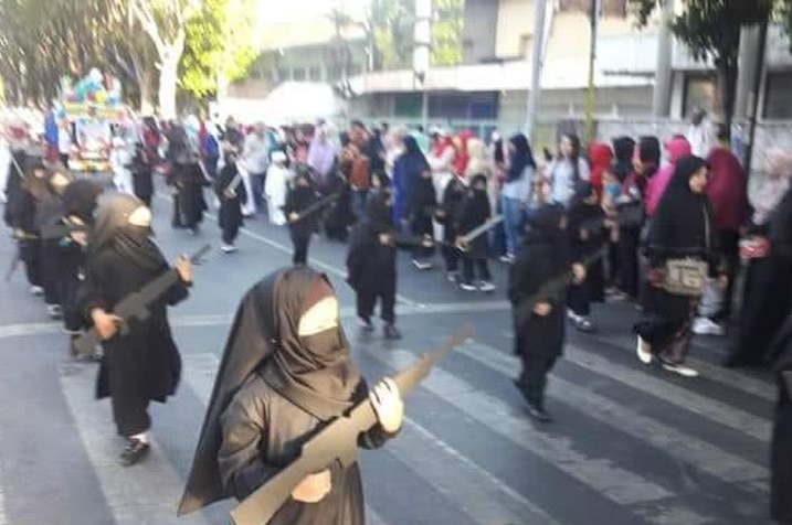 Children wearing a burqa and holding cut-out weapons in parade