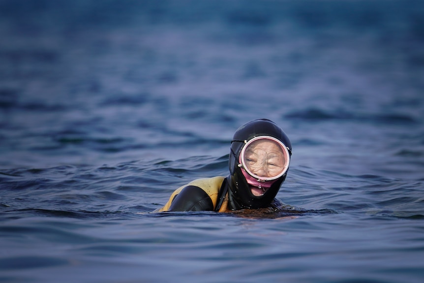 A woman wearing diving gear smiles while floating above the water in the ocean.