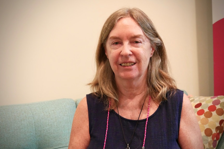 A mature women is sitting on a couch and smiling at the camera.