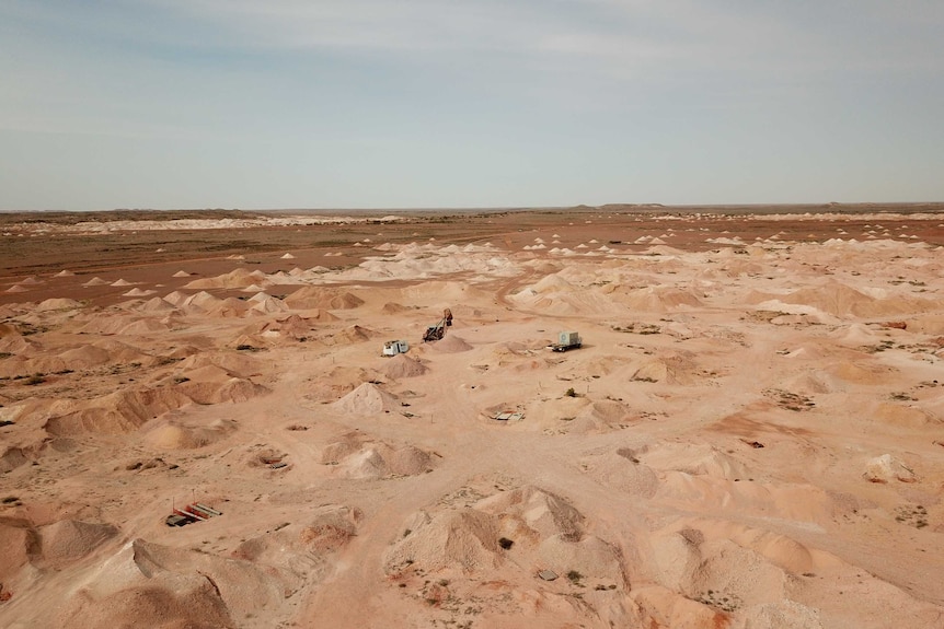 Mounds of red dirt stretch off into the horizon, with holes scattered across the field, which sits against a blue-grey sky.