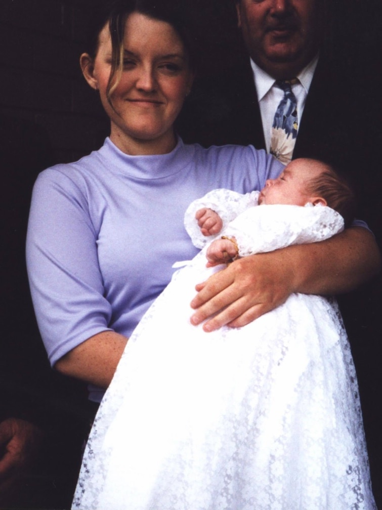 Bronwyn Fielding holds her baby, wearing a long white dress.