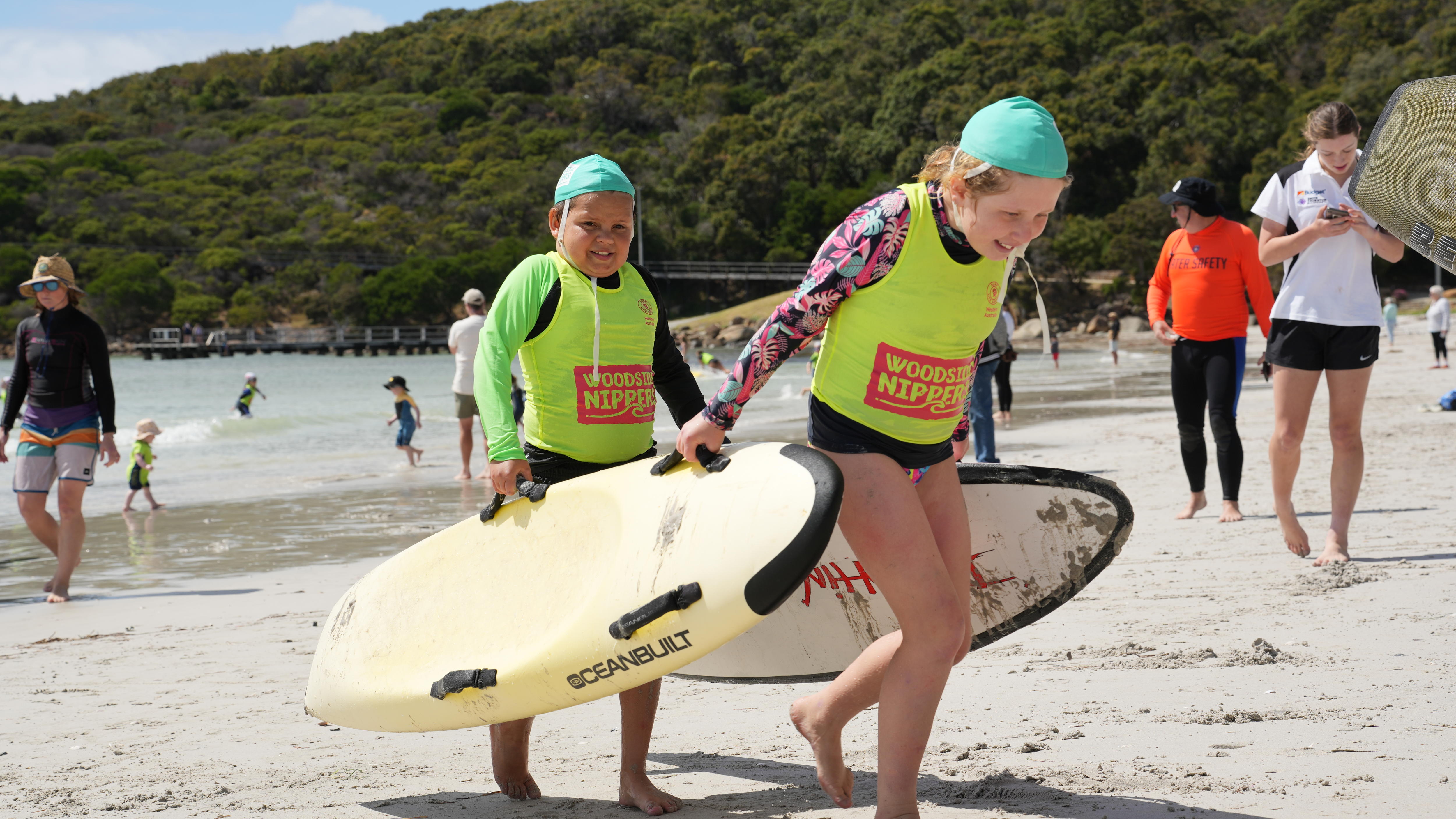 Un niño y una niña con uniformes de pinza se ayudan mutuamente a sacar tablas de surf del agua.