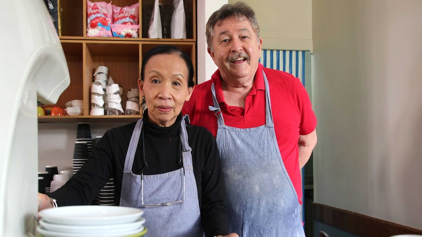 Delphine and Patrick Sullivan wearing aprons inside their cafe, with dishes blurred in the foreground.