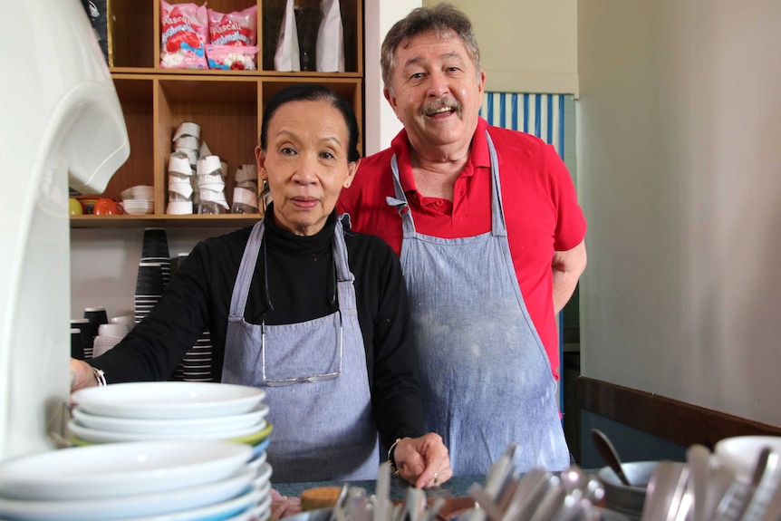 Delphine and Patrick Sullivan wearing aprons inside their cafe, with dishes blurred in the foreground.