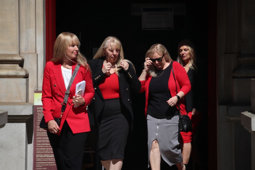 Four women leave a court building, with all of them wearing a piece of red clothing.