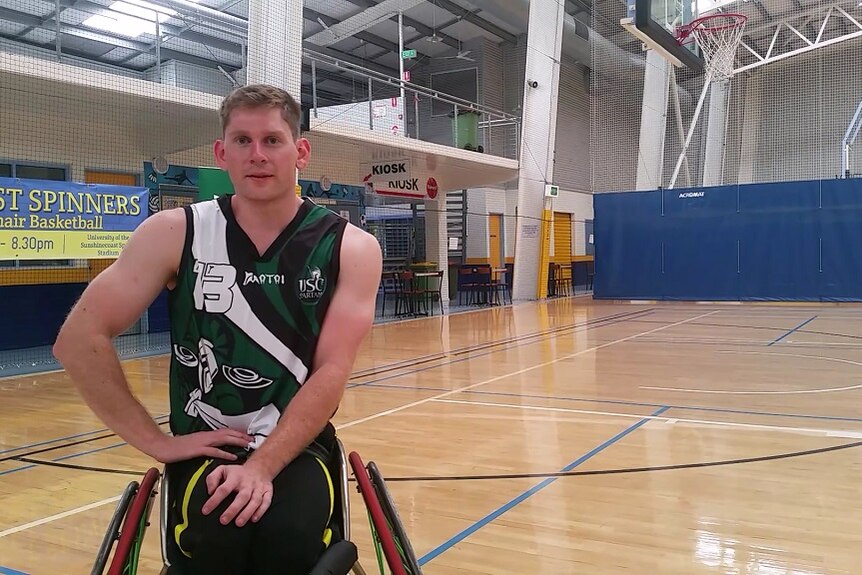 Man in his early 20s sitting in a wheelchair on a basketball court looking at the camera.
