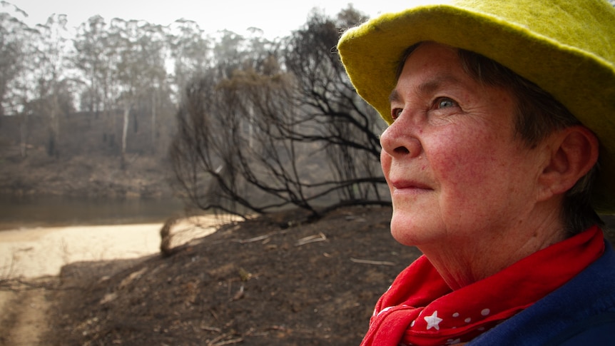 Side shot of woman looking up with burnt trees in the background.