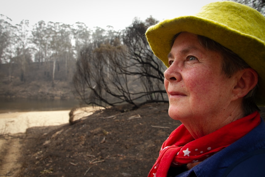 Side shot of woman looking up with burnt trees in the background.