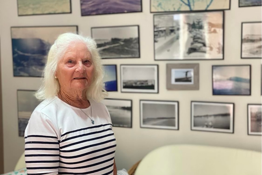 A woman with white hair standing in front of a wall of photos