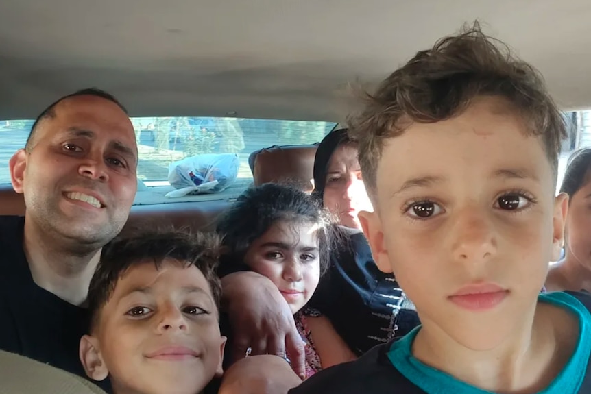 Hani is pictured smiling in the back of a car. There are children around him.