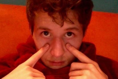A young man pulls his eyelids down with his index finger while looking into the camera.