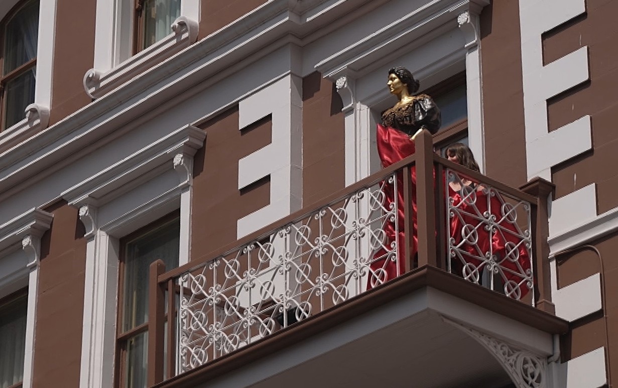 Estatua de bronce de una mujer en el balcón de un edificio.