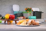A table with fruits and vegetables with open caddy bins in the background