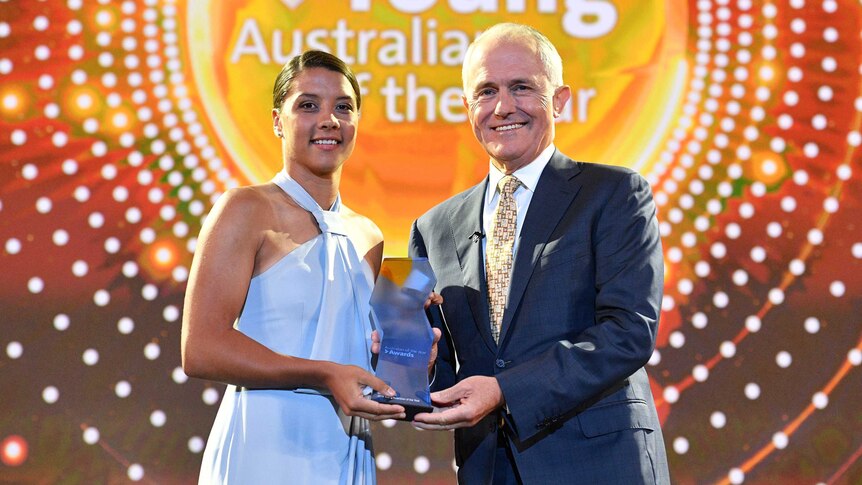 Sam Kerr stands on stage with Prime Minister Malcolm Turnbull with yellow sign behind them