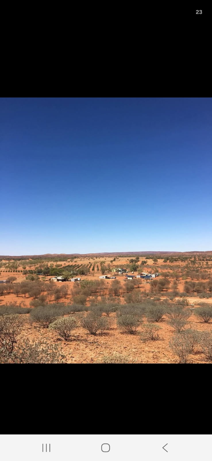 A landscape of orange dirt and low green bushed with a small cluster of houses in the distance