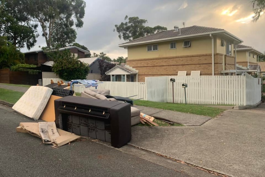 Bedding and furniture dumped on footpath outside a house.