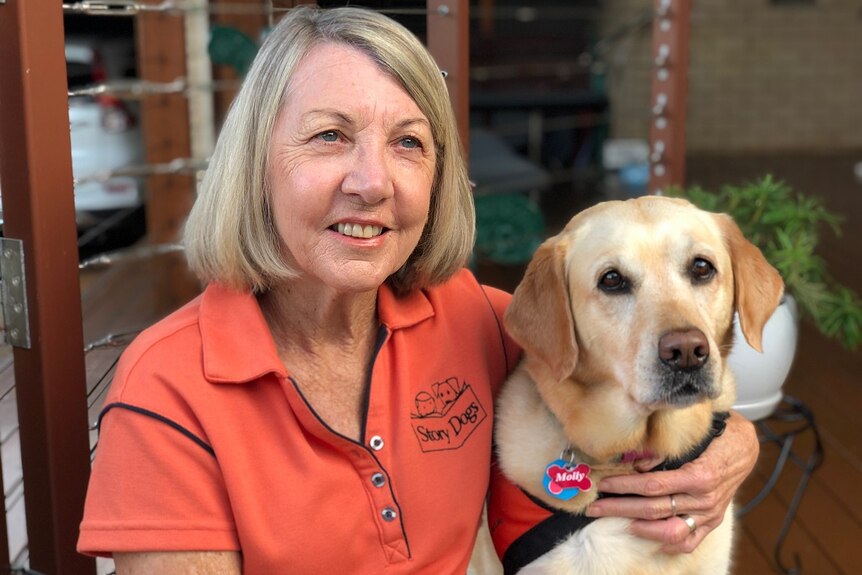 A smiling woman sits with her arm around her labrador dog.