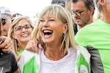 Olivia Newton-John is smiling and laughing, at the front of a crowd of runners at the Wellness Walk and Research Run.