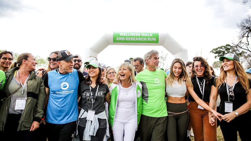 Olivia Newton-John is smiling and laughing, at the front of a crowd of runners at the Wellness Walk and Research Run.