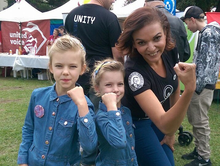 Anne Aly poses for a picture with two unidentified girls in front of outdoor stalls.