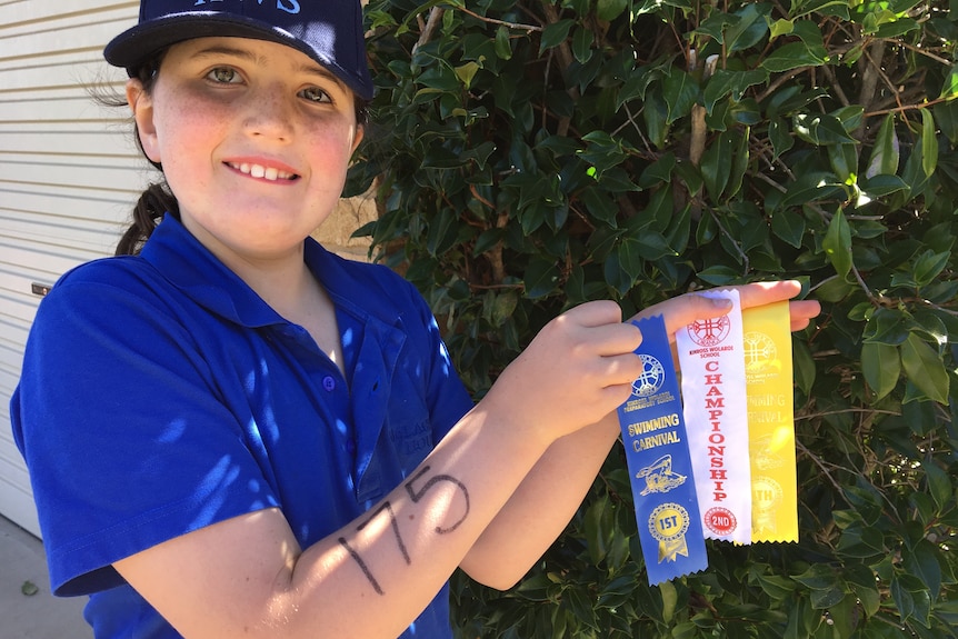 A young girl holding several sporting ribbons.