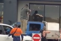 Screenshot of mobile phone footage, men holding guns pointed into the window of a ute.