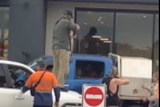 Screenshot of mobile phone footage, men holding guns pointed into the window of a ute.