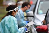 Healthcare workers in PPE talk to drivers through car windows at a drive-in testing centre in Melbourne