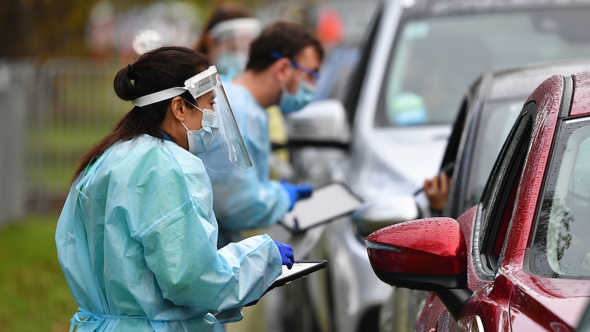 Healthcare workers in PPE talk to drivers through car windows at a drive-in testing centre in Melbourne