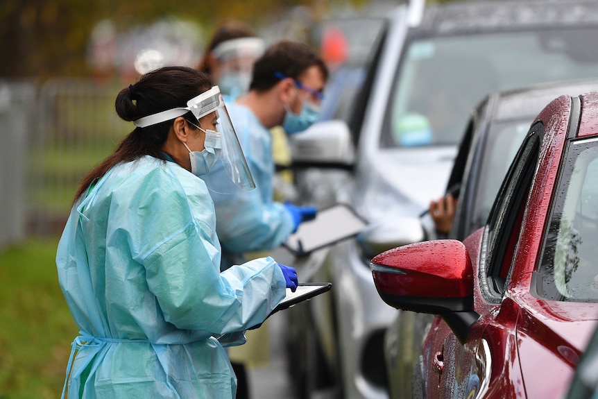 Healthcare workers in PPE talk to drivers through car windows at a drive-in testing centre in Melbourne