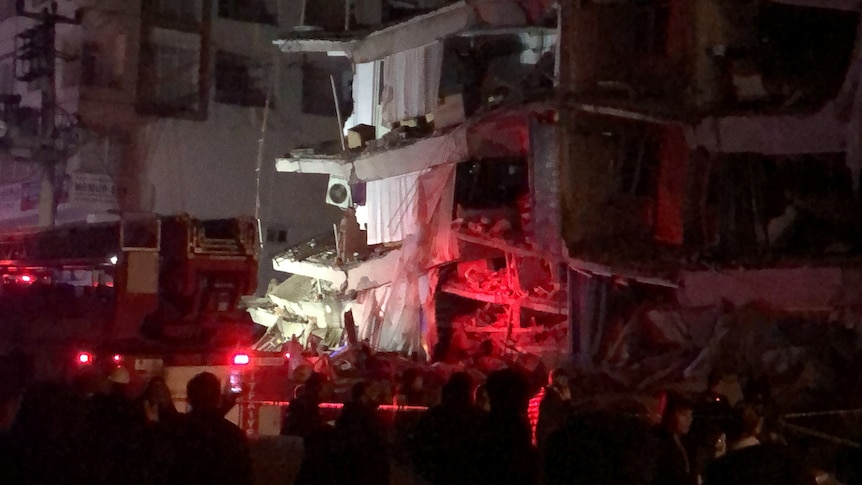 People gather near a building that collapsed in the early morning dark.