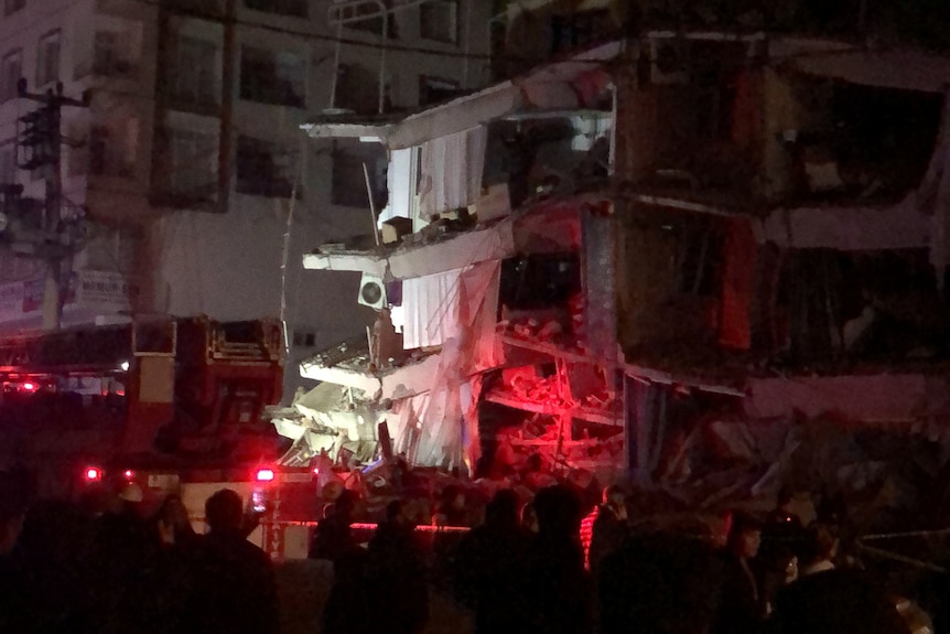 People gather near a building that collapsed in the early morning dark.