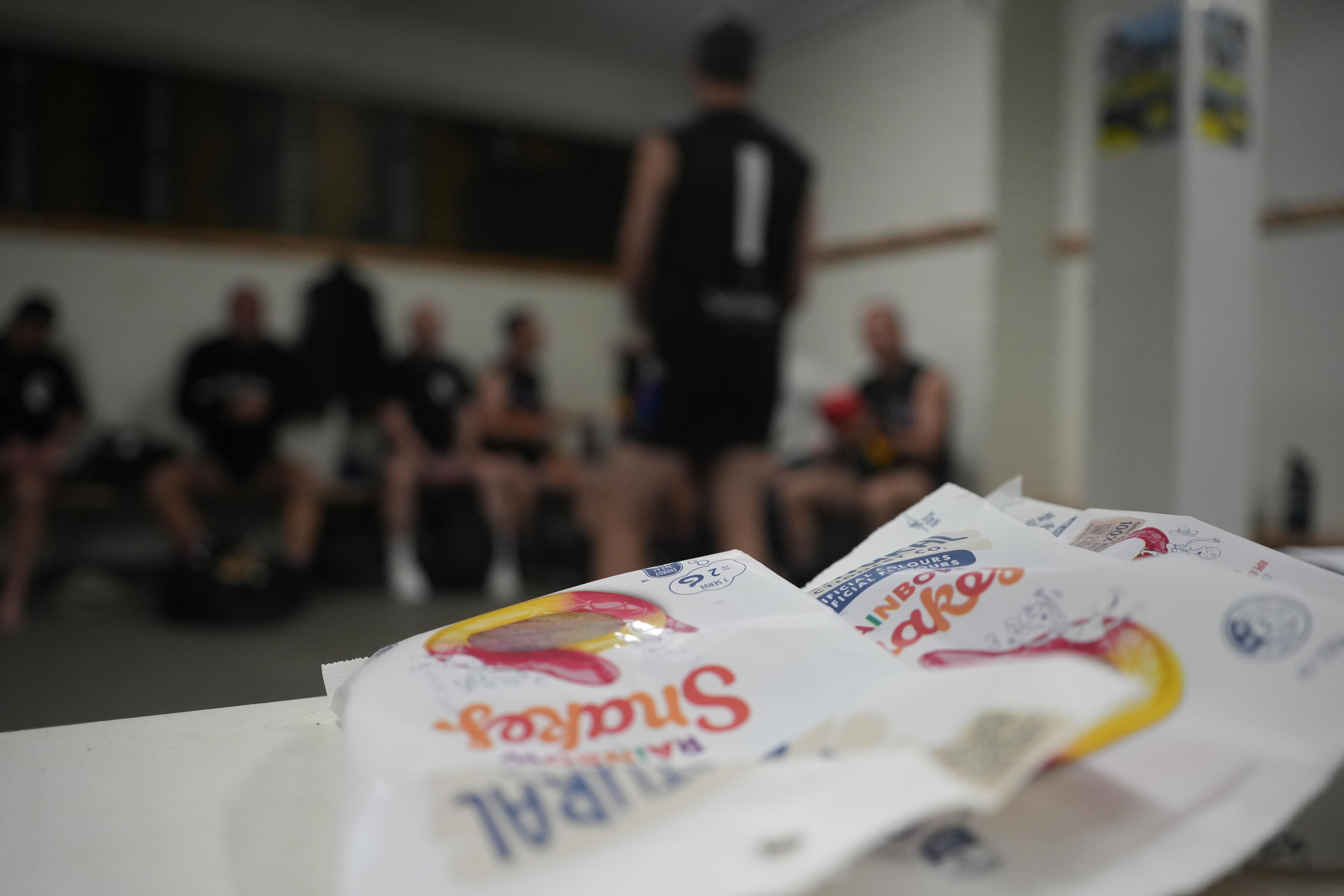 Three packets of lollies lie on a bench in the South Coast Sharks change rooms, with players getting ready in background