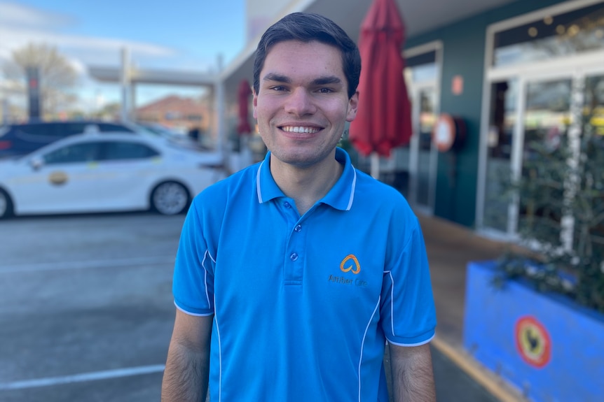 A man wearing a light blue polo shirt standing in a car park in front of a building