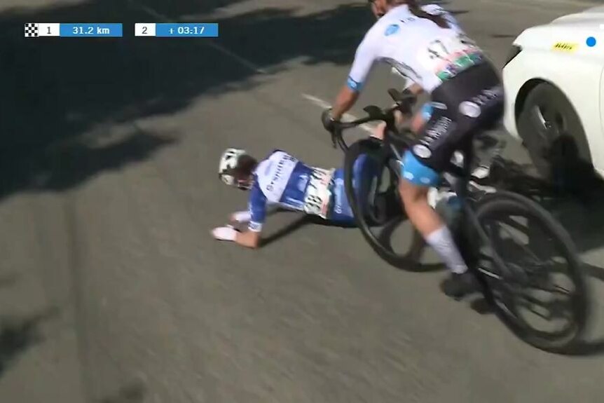 A cyclist on the ground in front of another racer. A car is next to the two riders.