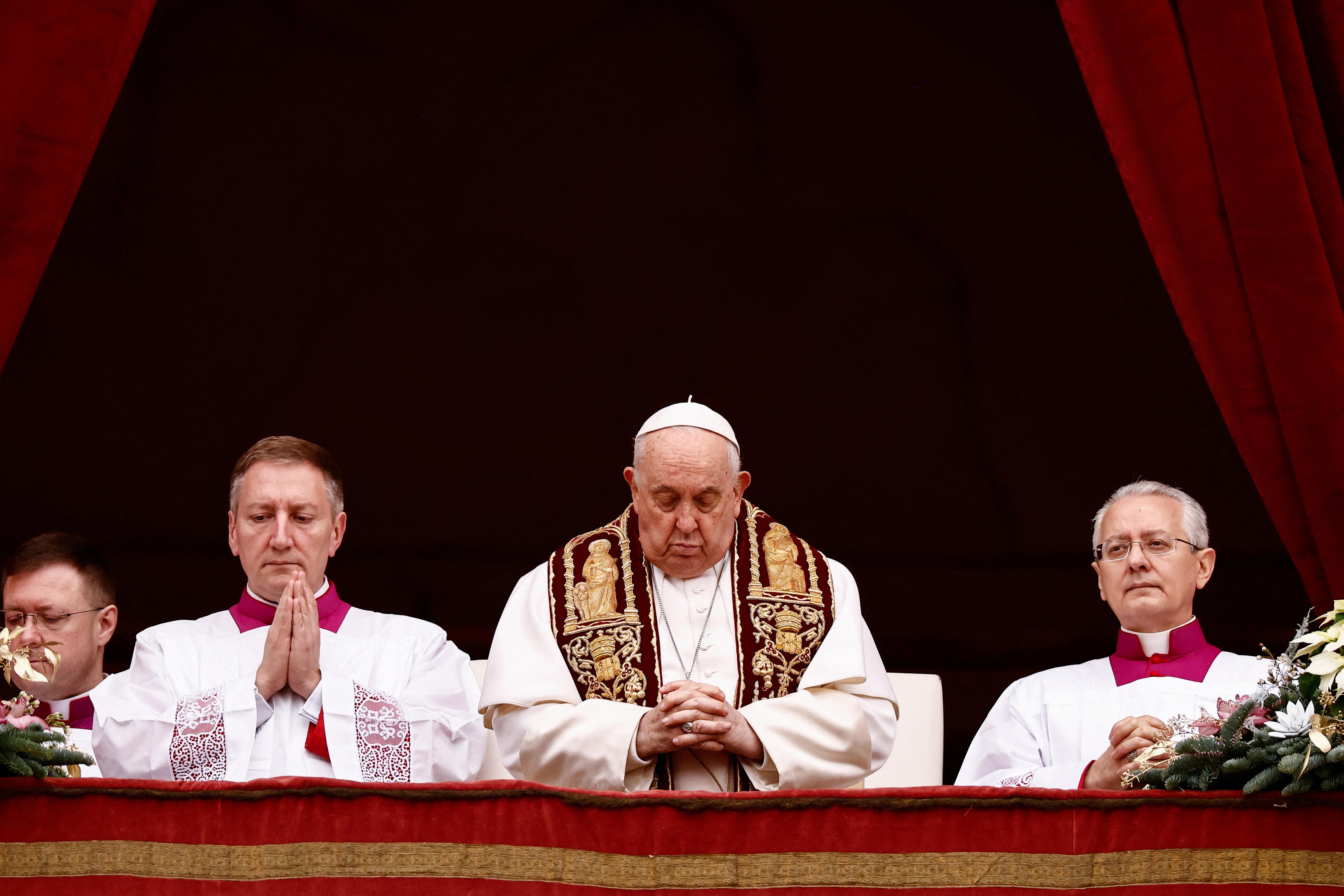 Pope Francis praying standing between two other praying men.