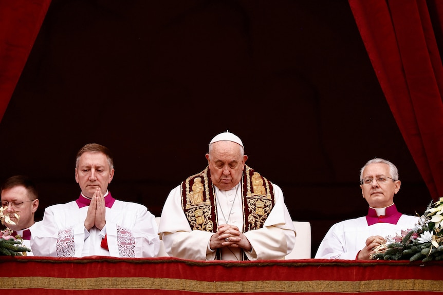 Pope Francis praying standing between two other praying men.