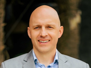 A bald man in a grey suit with a blue undershirt