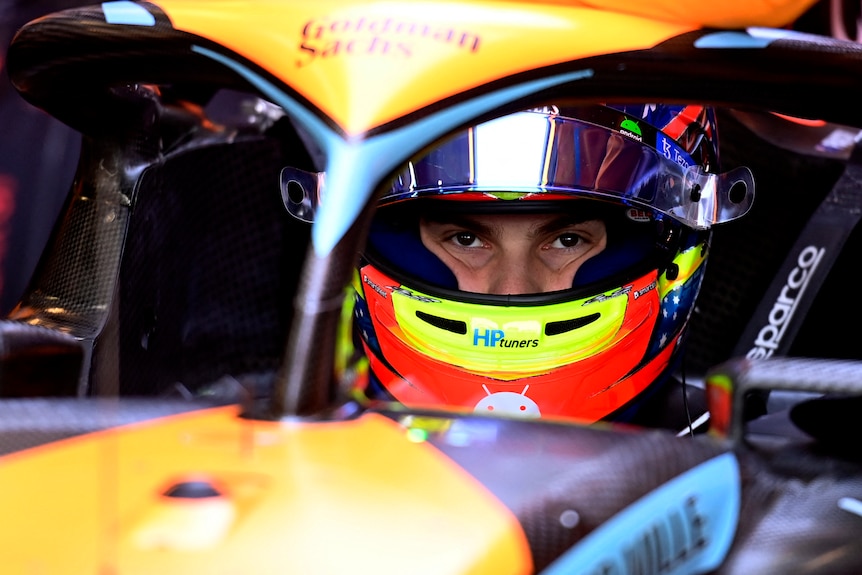 Le pilote de F1 Oscar Piastri s'abaisse dans sa voiture orange McLaren F1, portant sa combinaison de course complète, y compris un casque.