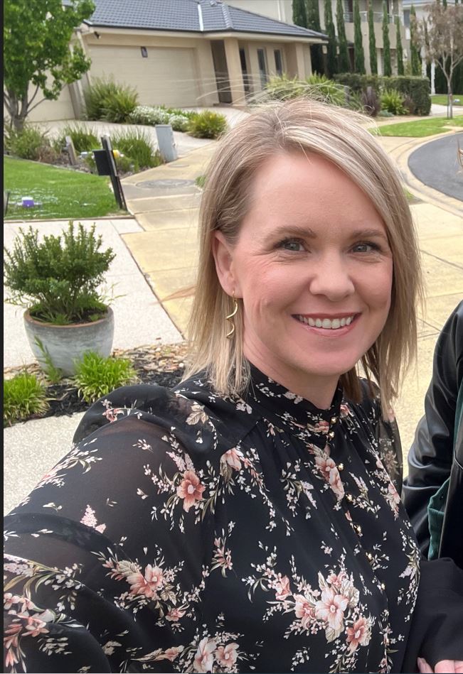Emma McGregor stands outside houses, smiling. She has shoulder-length blonde hair.