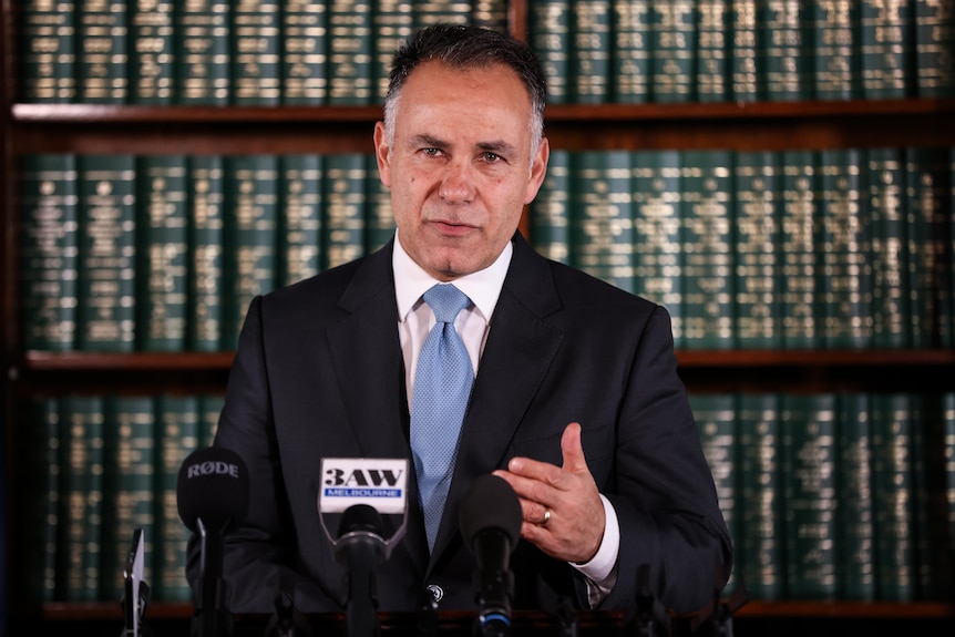 John Pesutto gestures as he speaks in front of a bookshelf filled with books.