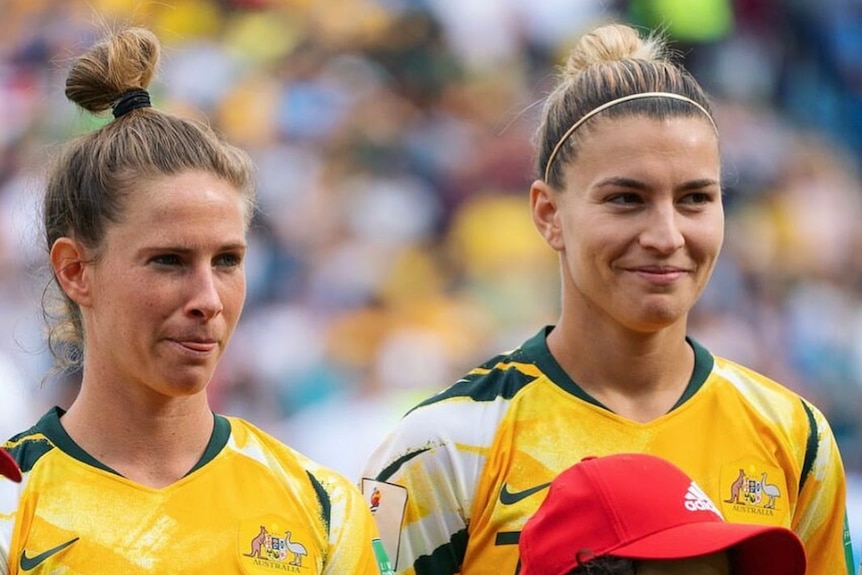 Steph Catley (right) stands proudly in her Australian jersey. She has a big smile on her face.