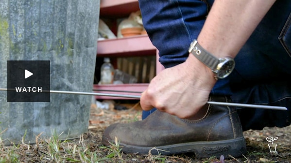 Hands holding metal rods being bent around bin. Has Video