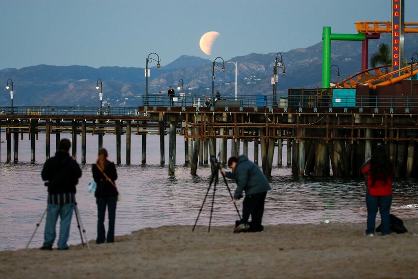 People take photos of the super blue blood moon at Santa Monica Beach.